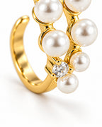 The Ilse Pearl Cluster Ring in observed gold finish, lower-setting macro view of a clear round faceted accent, petite gold prongs, pearl-like cabochons, and the open-band curve on a pearl-white background; reference-based AI visualization.