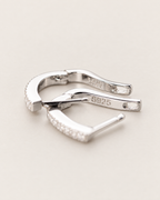 The Aria CZ Hoops — open polished silver-colored U-shaped hoop closures with partial clear stone edges on pale greige, reference-based AI visualization