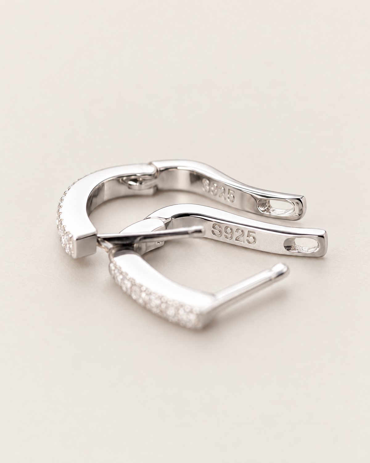 The Aria CZ Hoops — open polished silver-colored U-shaped hoop closures with partial clear stone edges on pale greige, reference-based AI visualization
