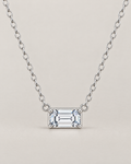 The Mara Geometric CZ Pendant — jewelry-only straight-on hero with a horizontal clear rectangular stone, four corner prongs, side connector rings, and an alternating-link chain on pale warm greige; reference-based AI visualization