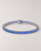 The Orla CZ Tennis Bracelet — complete low-angle silver-tone blue-stone tennis bracelet on pale greige — reference-based AI visualization