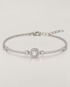 The Sora Halo Bracelet polished cool silver-tone complete low-angle resting lay with clear-stone halo, slender curved stone-set bars and chain extension on pale greige reference-based AI visualization