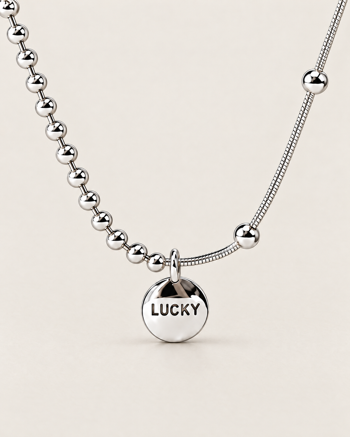 Front macro detail of the round LUCKY medallion, oval bail, and adjacent silver-colored beaded and smooth station-bead chain sections, reference-based AI visualization