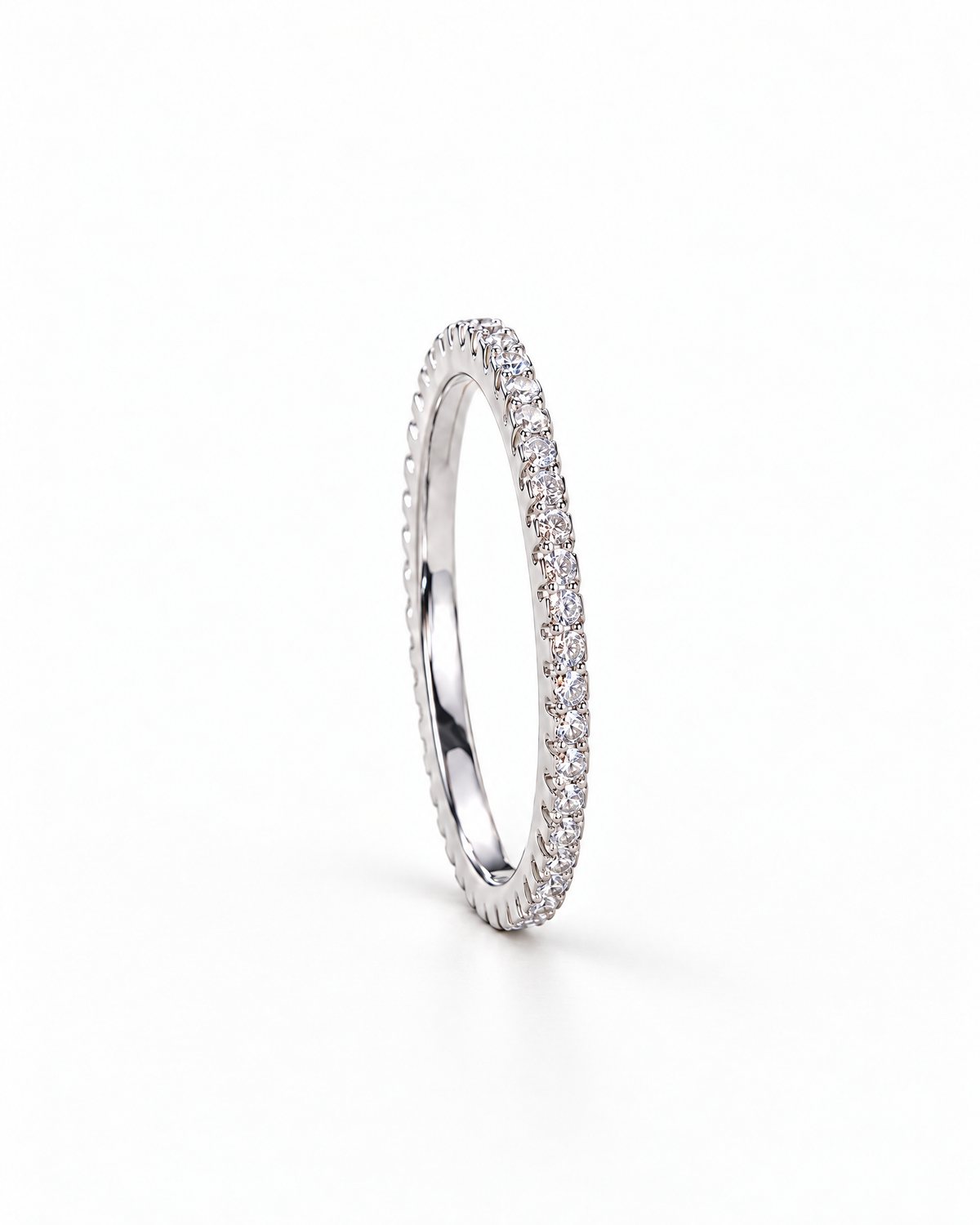 The Vale CZ Eternity Band — bright polished silver-tone clear-stone eternity band in a side setting profile on a pearl-white studio background, reference-based AI visualization