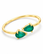 The Tove Green Twin-Pear Ring in polished yellow-gold coloured metal with two green pear-cut stones in a diagonal front detail on a pearl-white studio background, reference-based AI visualization.