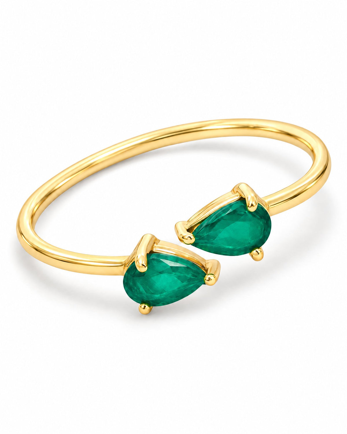 The Tove Green Twin-Pear Ring in polished yellow-gold coloured metal with two green pear-cut stones in a diagonal front detail on a pearl-white studio background, reference-based AI visualization.