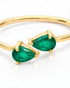 The Tove Green Twin-Pear Ring in polished yellow-gold coloured metal with paired green pear-cut stones in a close setting macro on a pearl-white studio background, reference-based AI visualization.