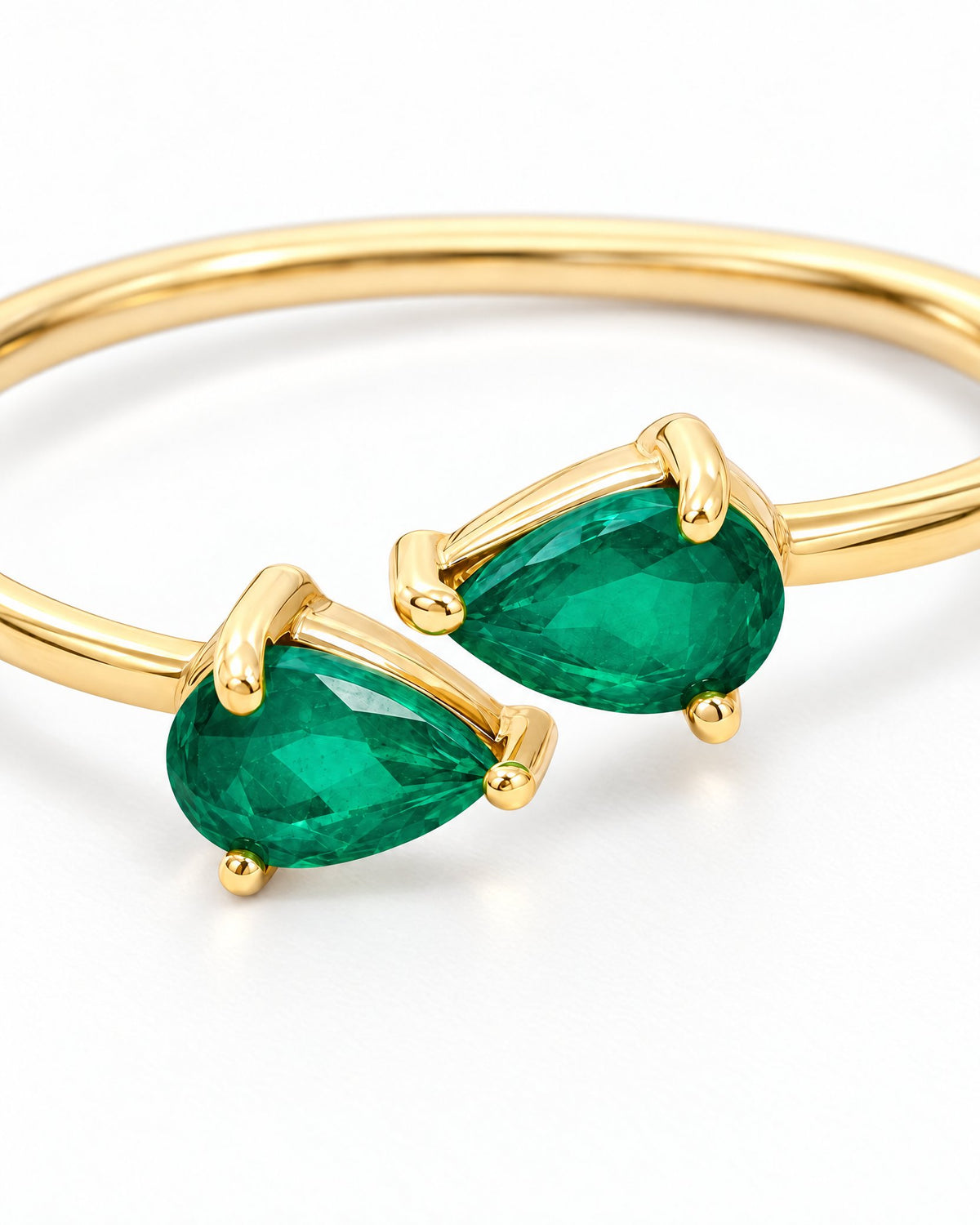The Tove Green Twin-Pear Ring in polished yellow-gold coloured metal with paired green pear-cut stones in a close setting macro on a pearl-white studio background, reference-based AI visualization.