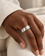 The Lena Hammered Open Band Ring — polished silver-tone hammered open band worn on a deep-brown hand against ivory linen, reference-based AI visualization.