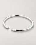 The Talo Open Cuff Bangle — polished silver-tone open oval with documented latch gap and hinge seam on pale greige; reference-based AI visualization