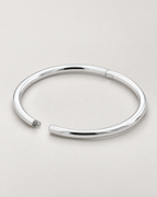 The Talo Open Cuff Bangle — polished silver-tone open oval with documented latch gap and hinge seam on pale greige; reference-based AI visualization