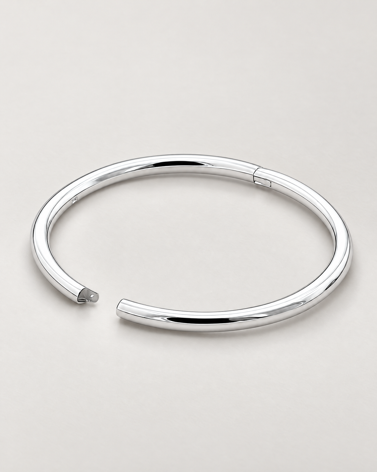 The Talo Open Cuff Bangle — polished silver-tone open oval with documented latch gap and hinge seam on pale greige; reference-based AI visualization