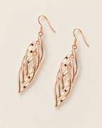 The Sova CZ Drop Earrings — Warm gold-color openwork leaf drop pair in a separated mirrored flat lay on pale greige; reference-based AI visualization