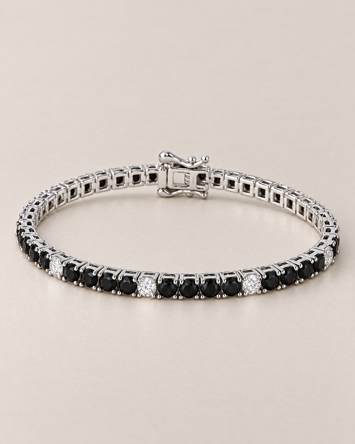 The Signe Black & White CZ Tennis Bracelet in polished silver-tone metal, shown in a low resting oval with repeating black and clear/white round stones and a box clasp on pale greige, reference-based AI visualization.