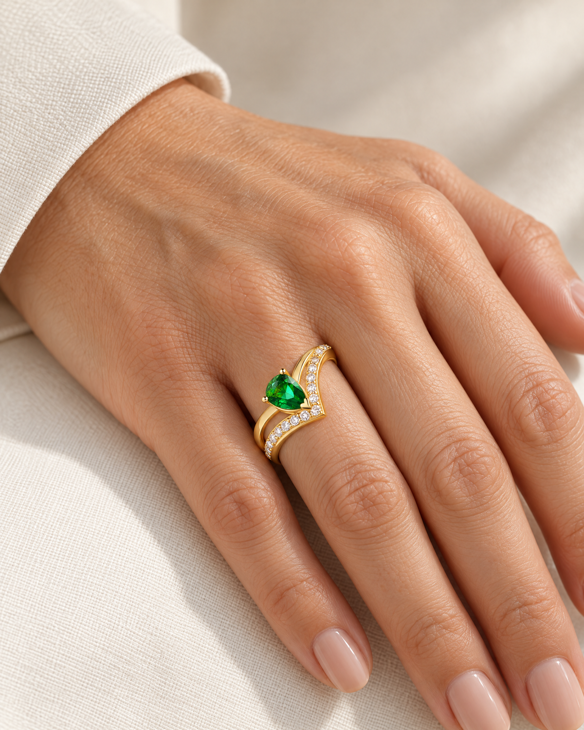 The Tuva Green Pear Wrap Ring in polished gold-color metal with a green pear-shaped stone and clear round accents worn on an adult woman's hand against ivory linen, reference-based AI visualization