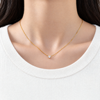 Gold-color necklace in a complete diagonal oval lay with its clear round four-prong stone, lobster clasp, extension links, and smooth end tag on pale warm greige; reference-based AI visualization.