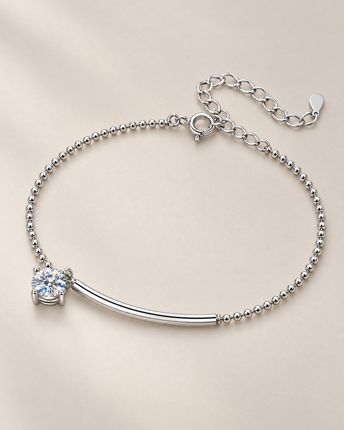 The Eden Moissanite Bracelet in polished silver tone, arranged as a full loop with a curved bar, one round clear stone, ball-bead chain, and extension clasp on a pale-greige background, reference-based AI visualization.