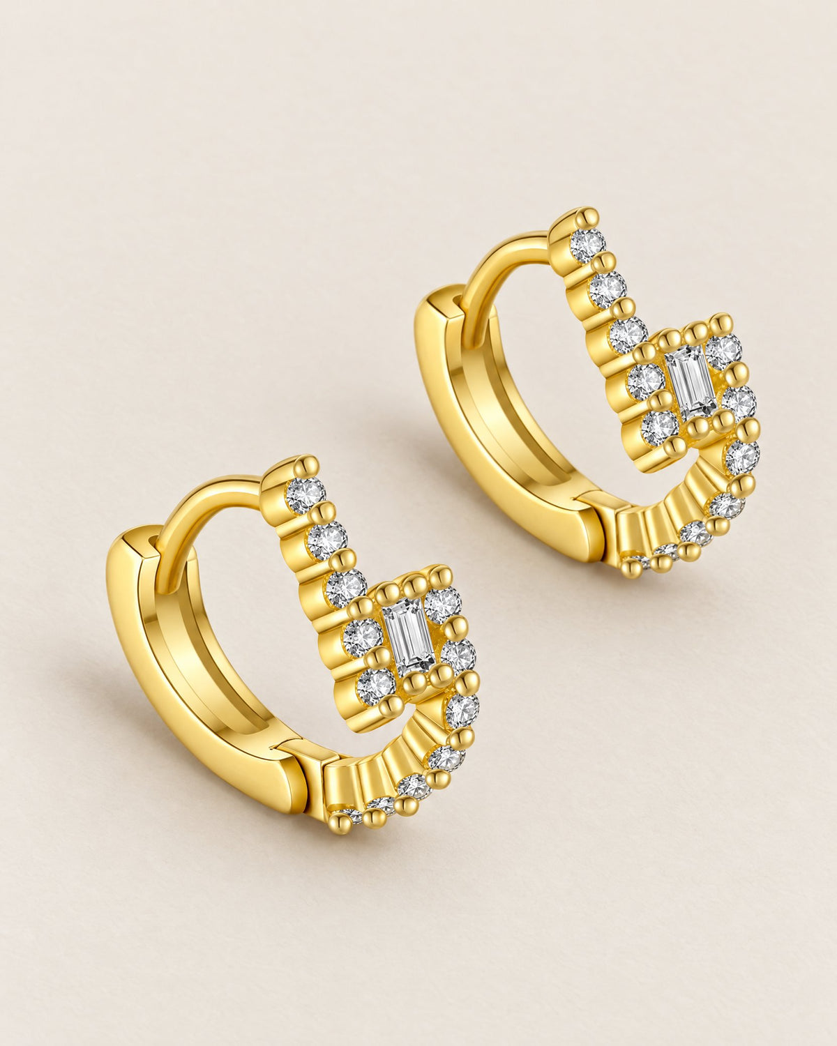 The Veyra Geometric Huggies, two warm yellow-gold-coloured geometric huggies in a low-angle diagonal resting arrangement with clear rectangular and round stones on pale greige, reference-based AI visualization