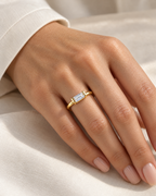 The Lyra CZ Emerald-Cut Statement Ring — gold-color clear emerald-cut ring worn on a relaxed light-warm adult hand with ivory linen; reference-based AI visualization.