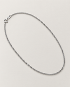 The Erin Fine Curb Chain Necklace — Sterling Silver complete diagonal oval curb-chain lay with spring-ring clasp and oval tag on pale greige, reference-based AI visualization.