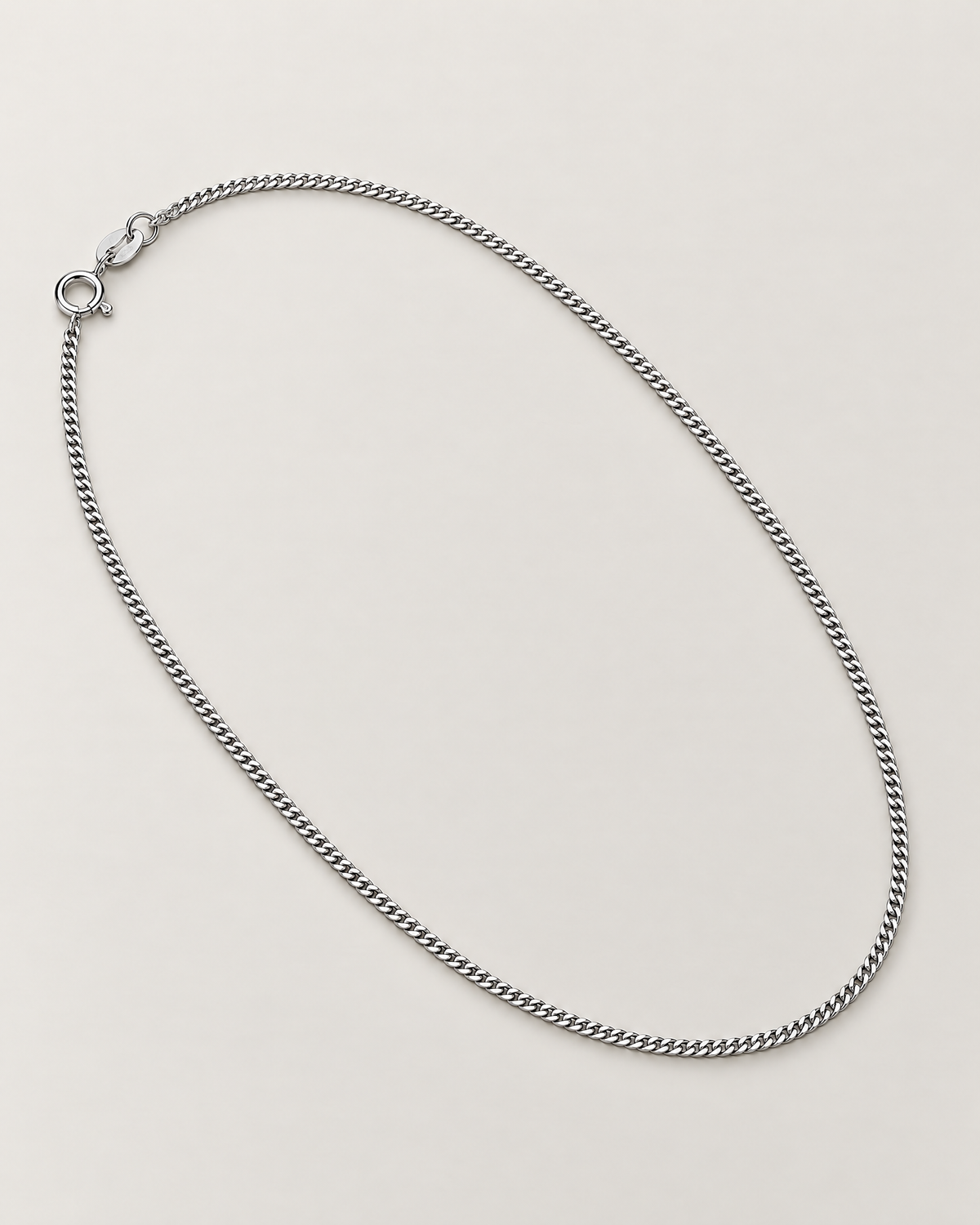 The Erin Fine Curb Chain Necklace — Sterling Silver complete diagonal oval curb-chain lay with spring-ring clasp and oval tag on pale greige, reference-based AI visualization.