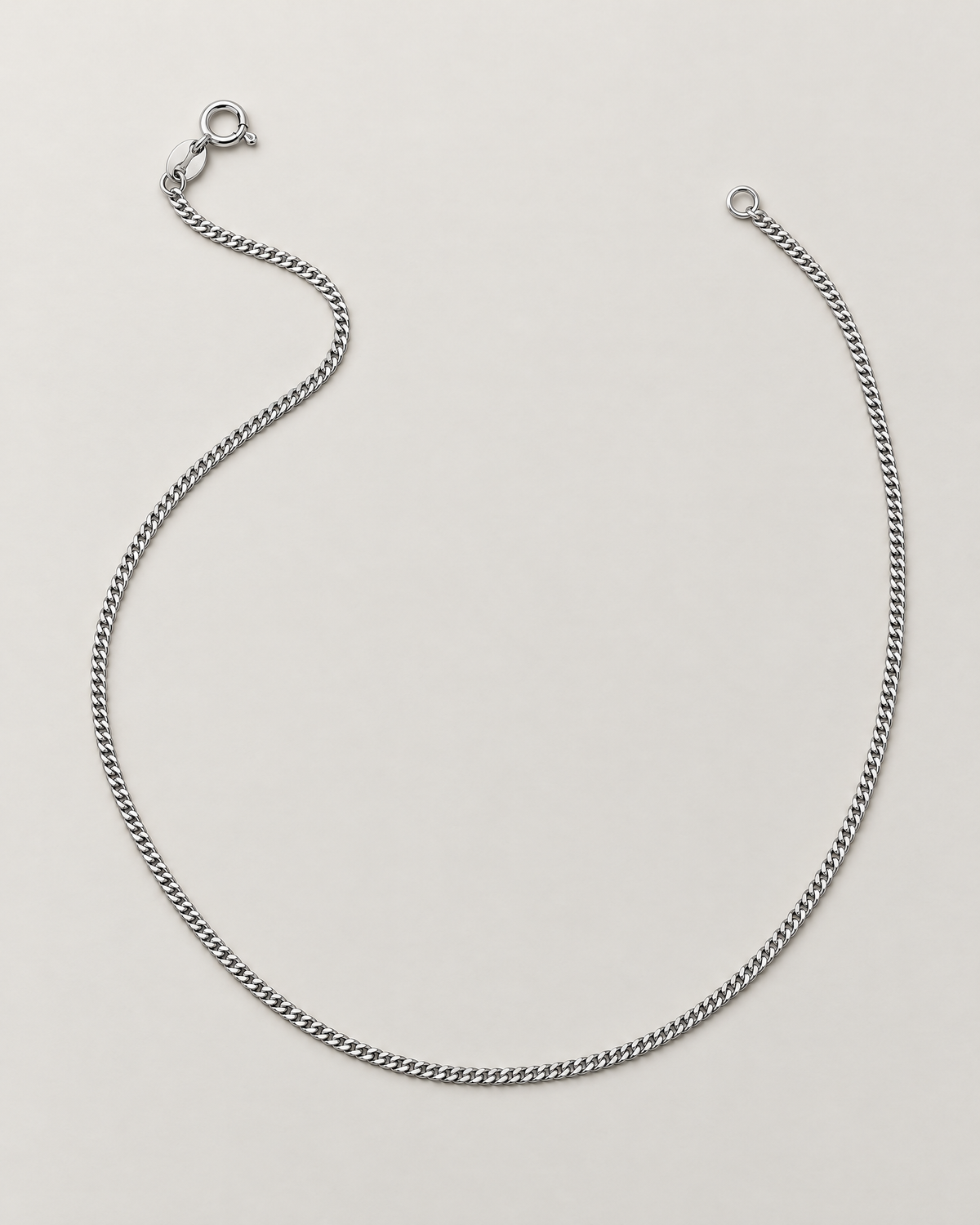 The Erin Fine Curb Chain Necklace — Sterling Silver complete relaxed flowing open-U curb-chain lay with spring-ring clasp and oval tag on pale greige, reference-based AI visualization.