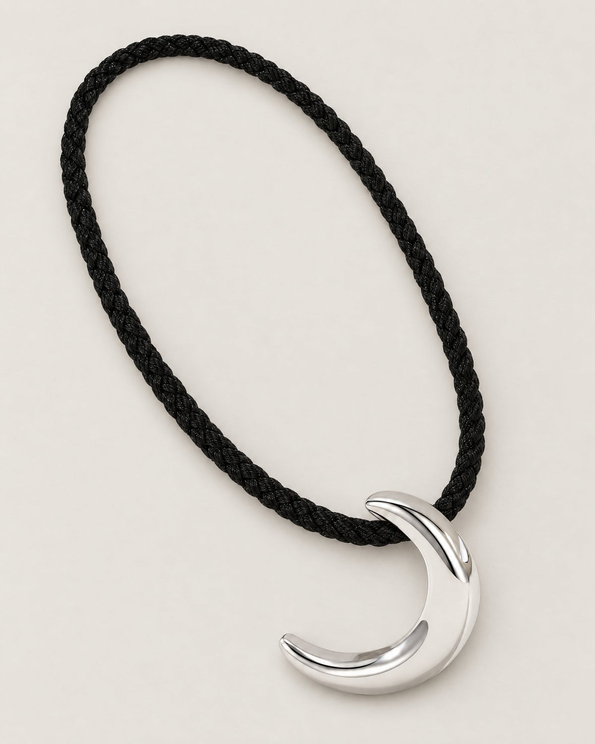 Black braided cord arranged in a diagonal oval around a polished crescent pendant on pale greige, reference-based AI visualization