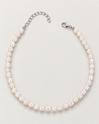Irregular off-white pearl strand arranged in an open horseshoe with separated clasp and extension ends on a pale greige studio surface; reference-based AI visualization